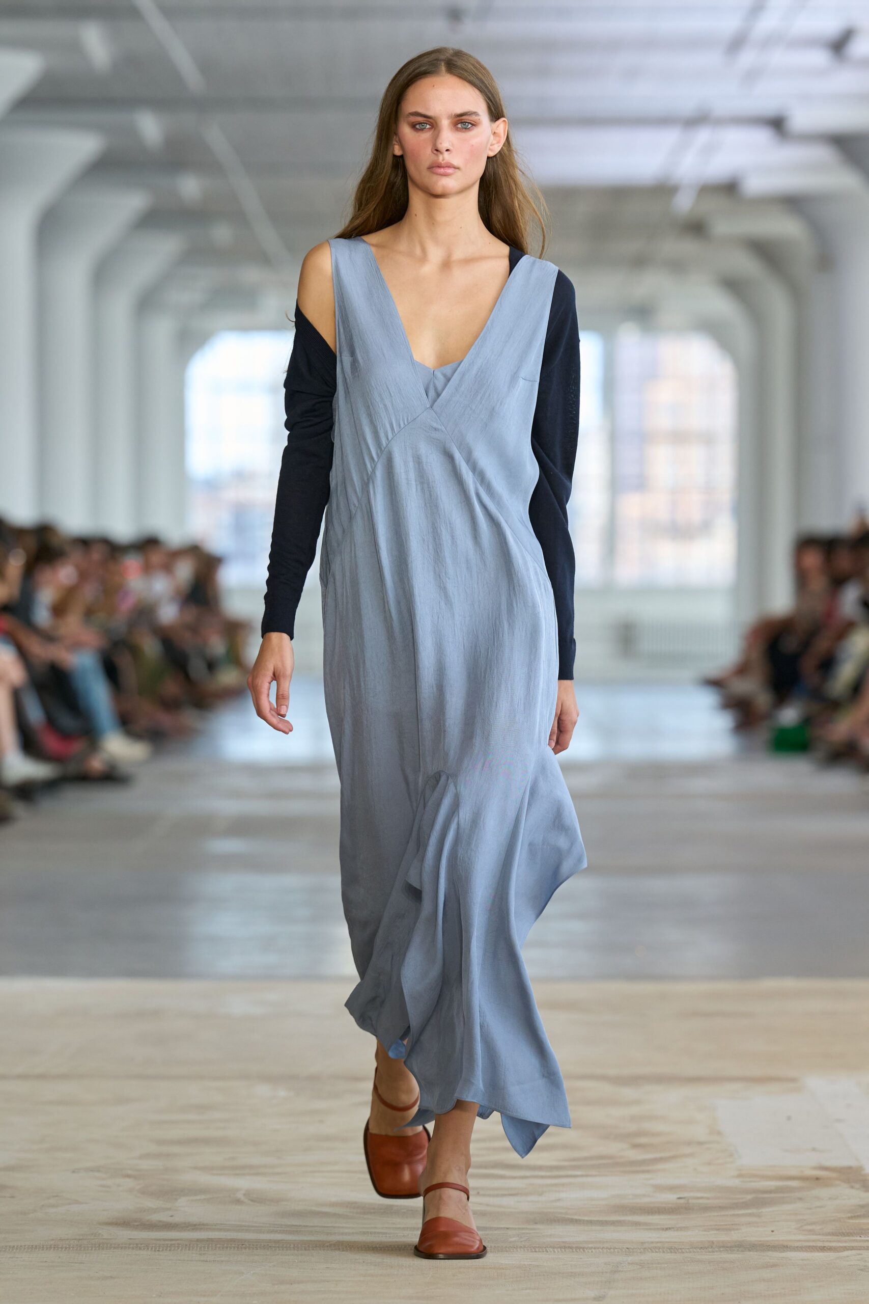 Powder-blue satin dress with a wrapped V front and skewed seam. Black knit sleeves worn slipping off both shoulders. Cognac square-toe flats with a slim instep strap. Crossing a quiet museum atrium before the air-conditioning wakes up.