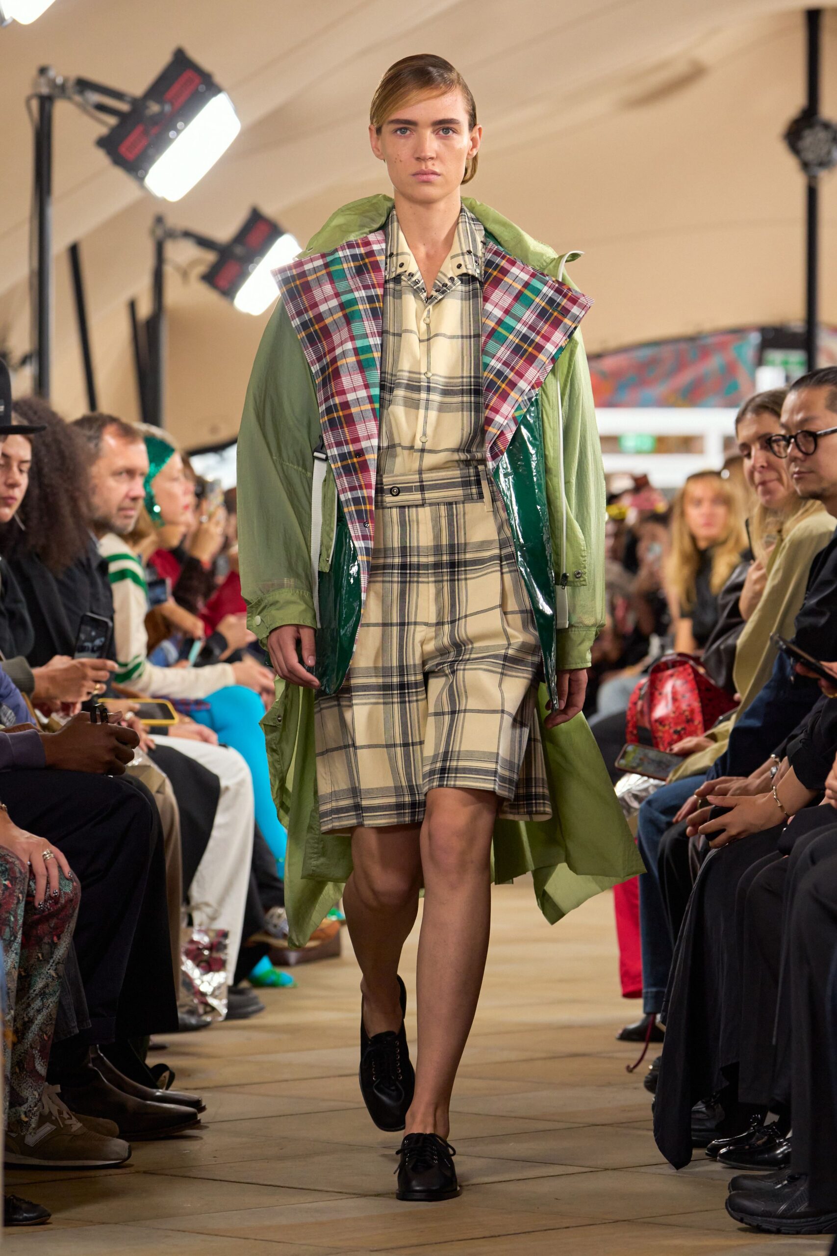 Pale pistachio parka with glossy green vinyl facings and a huge plaid lapel. Cream windowpane shirt dress, button tab cinching the waist slightly off center. Black leather derbies with plain round toes. Walking across wet grass after the village fete tents have come down.