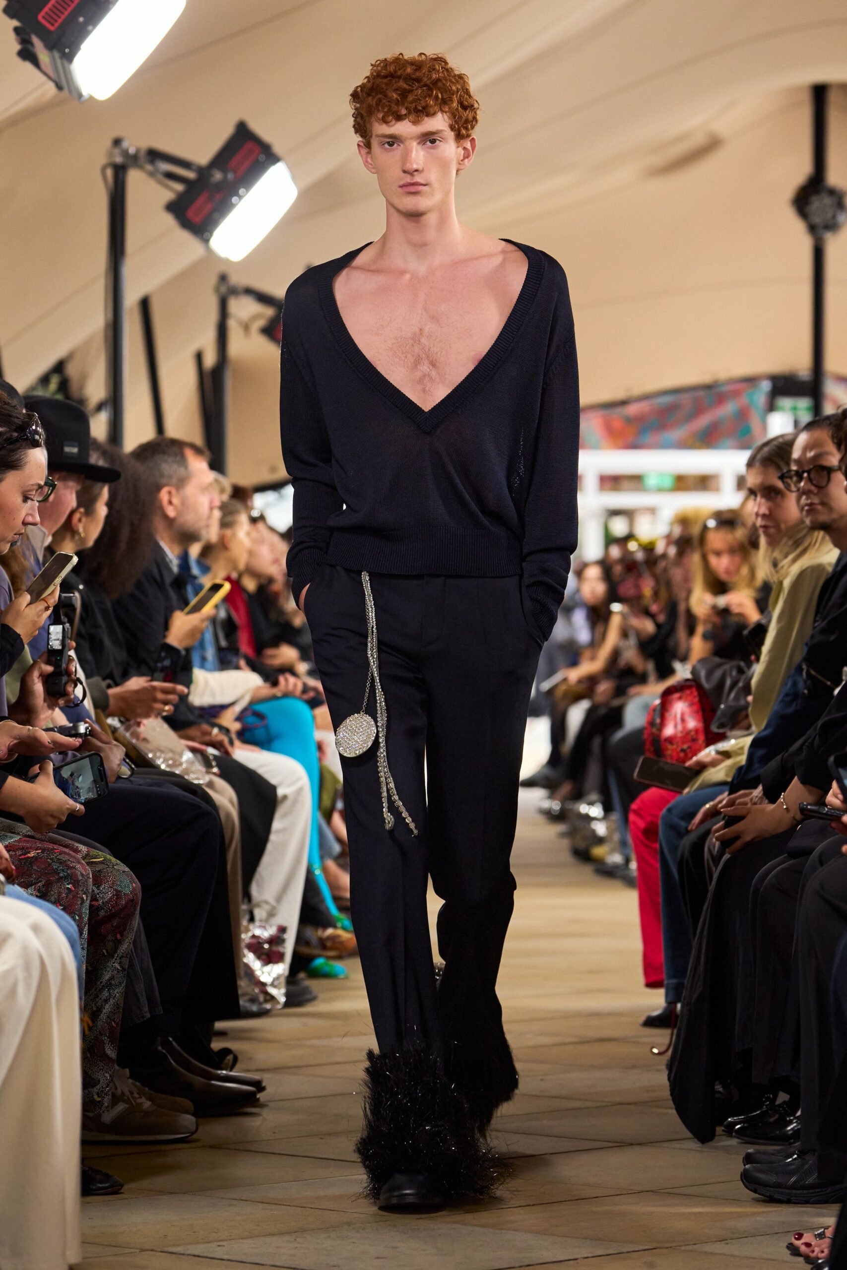 Deep navy knit sweater with a plunging V scooped off both shoulders. Black tailored trousers with a rhinestone coin purse swinging from the hip. Black boots swallowed by shaggy feather cuffs at the ankle. Walking into a hotel ballroom after midnight with nothing useful in the bag.