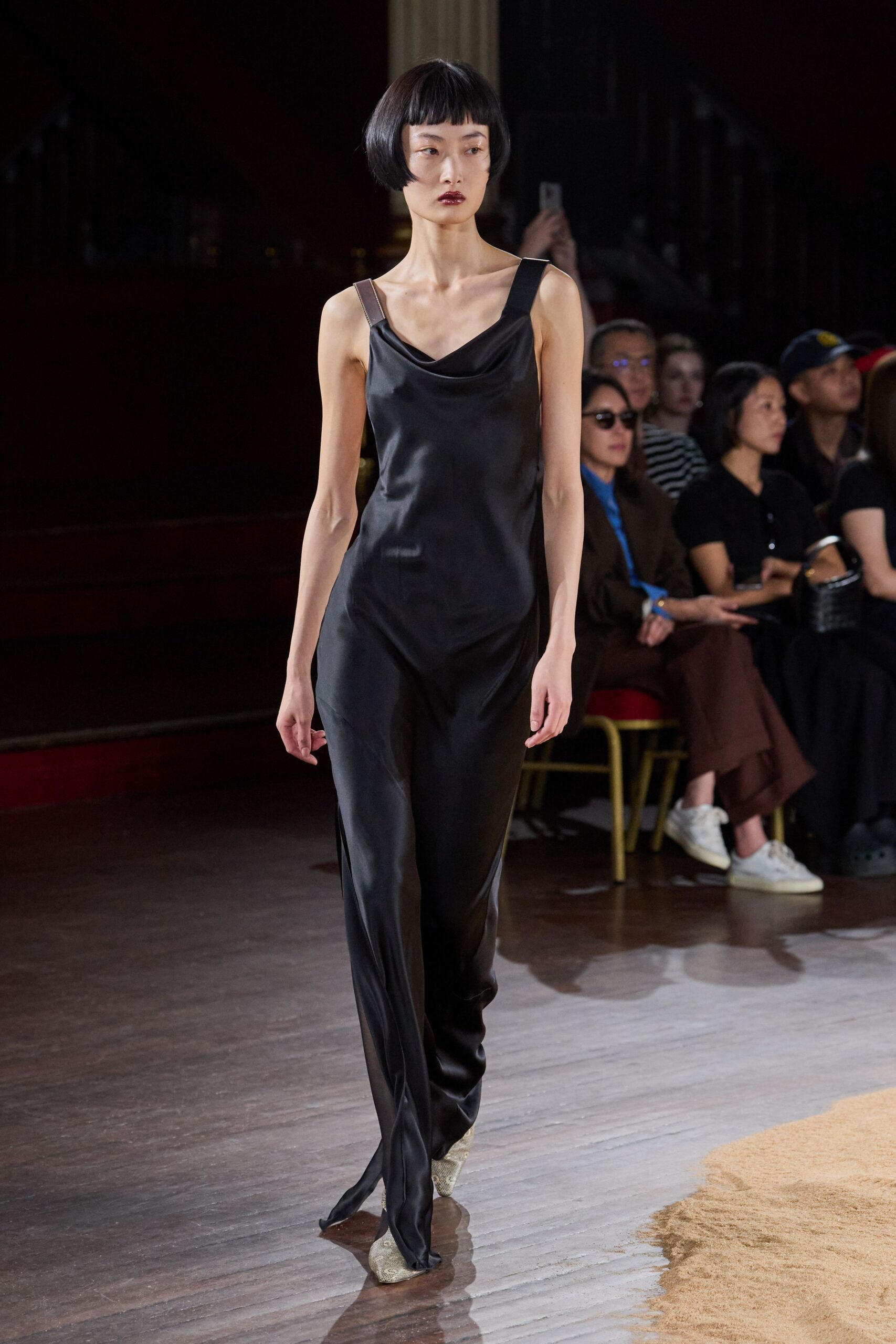 Black satin jumpsuit with a soft cowl neck and split hems. Mismatched shoulder straps, one black and one cocoa brown. Python pointed boots peeking from the trouser break. Crossing a hotel ballroom before the chairs are stacked.