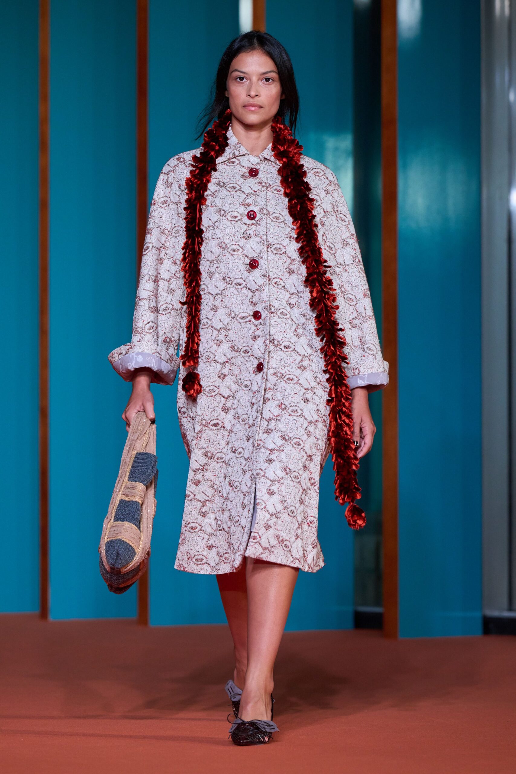 Cream coatdress in tapestry jacquard, set with glossy oxblood dome buttons. Long chenille scarf in crushed garnet velvet. Flat woven tote with two charcoal blocks and frayed rope edging. Black lattice flats tied with pale grey bows. Walking back from a beach hotel shop with postcards and sun still on your shoulders.
