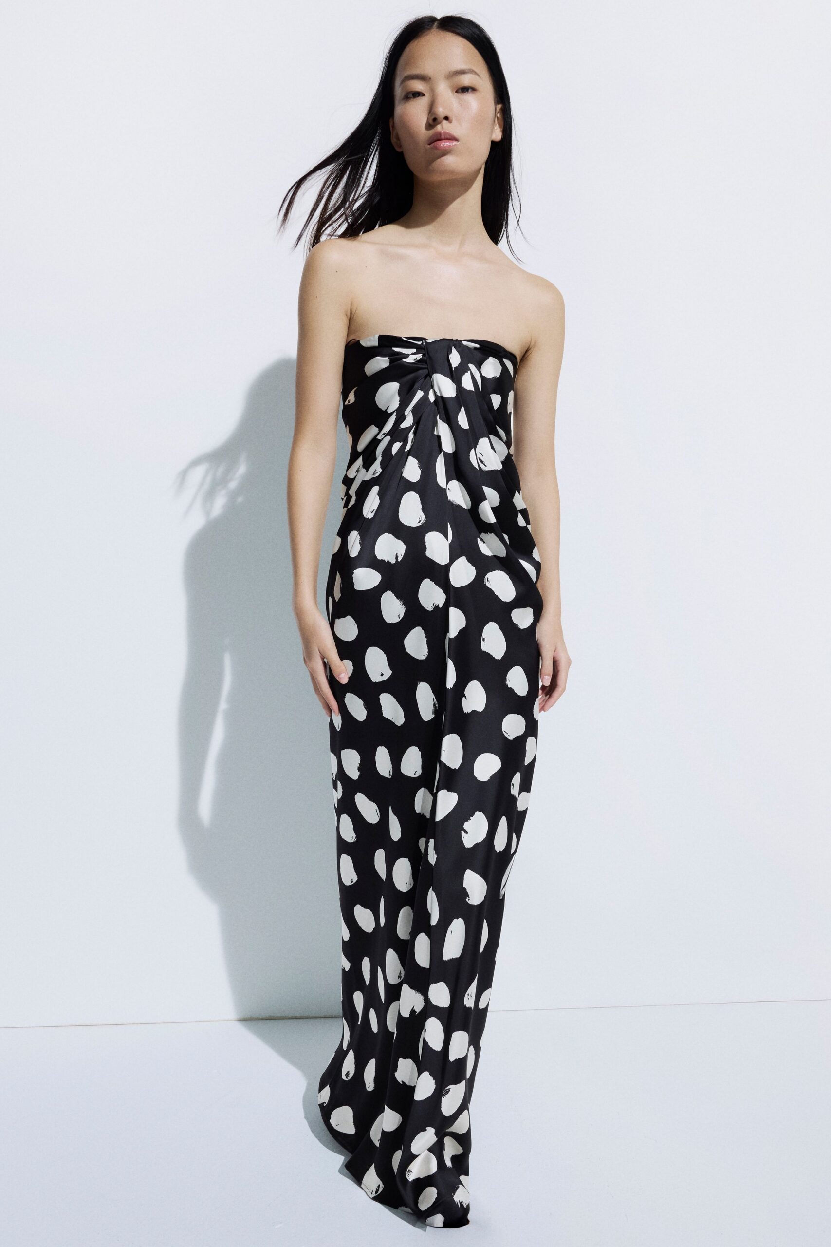 Strapless black satin jumpsuit splashed with white brushstroke dots, twisted at the bust. Heat bouncing off white concrete just after the pool has emptied.
