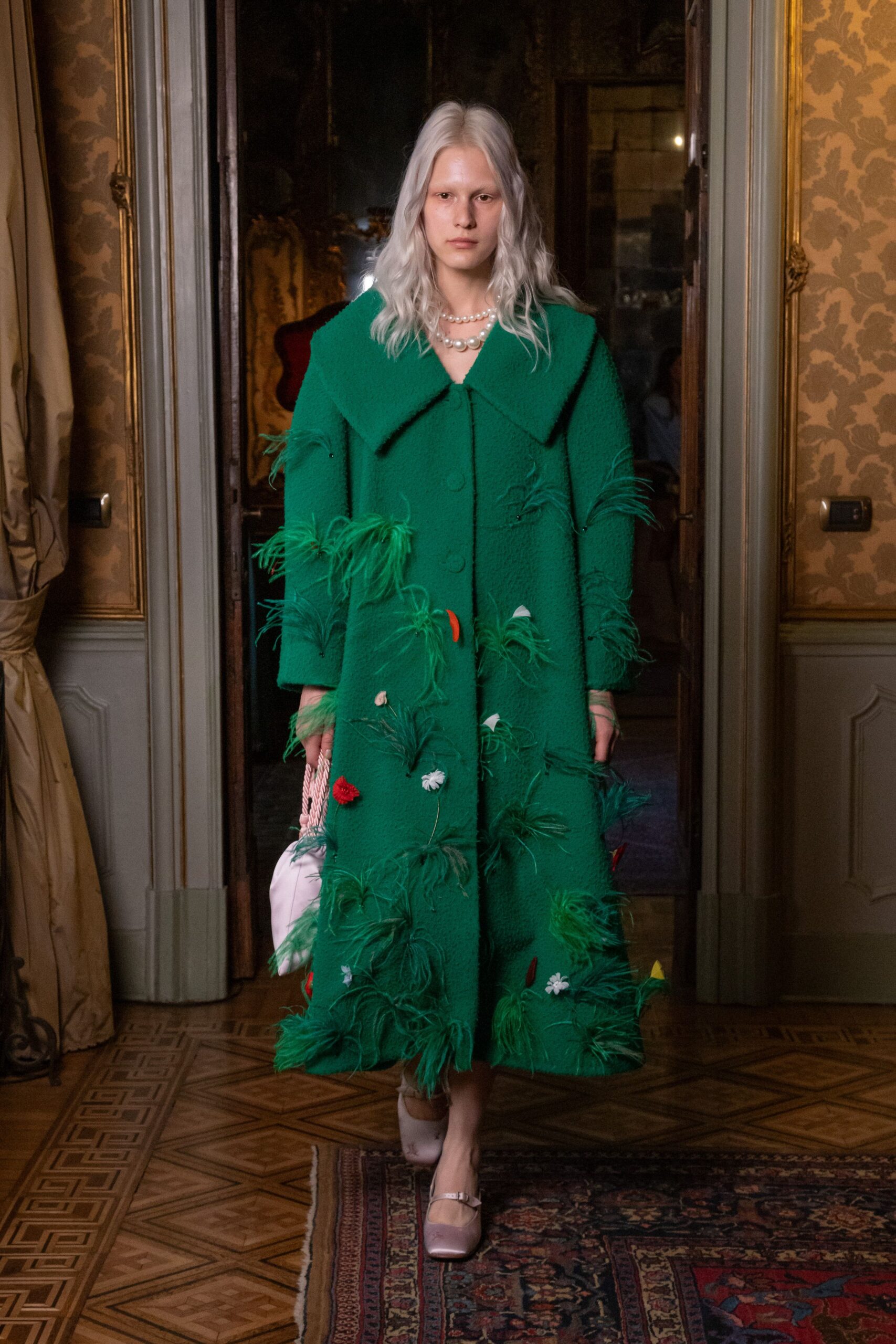 Emerald boucle coat with huge sailor collar, dotted in ostrich plumes and tiny flowers. Layered pearls with one oversized central bead. White ruched drawstring bag with thick twisted cords. Pale satin Mary Janes with a narrow instep strap. Crossing a carpeted salon after knocking over the arrangement yourself.