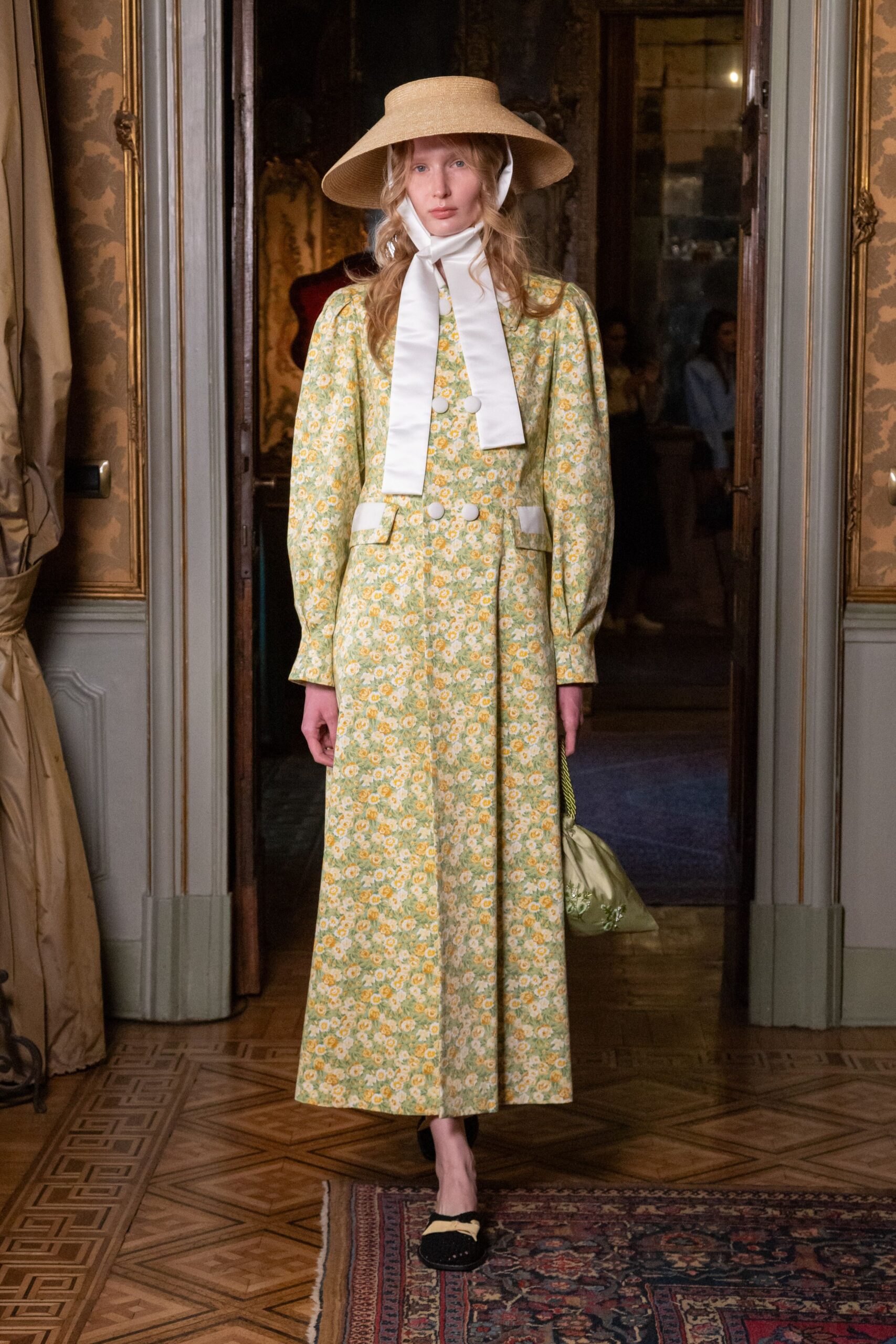 Wide straw sunhat tied under the chin with long white satin ribbons. Pale green floral dress with puffed sleeves, white flap pockets and covered buttons. Sage satin drawstring pouch with white floral embroidery. Black velvet slippers topped with a prim yellow bow. Crossing a parquet salon before tea is carried into the garden.