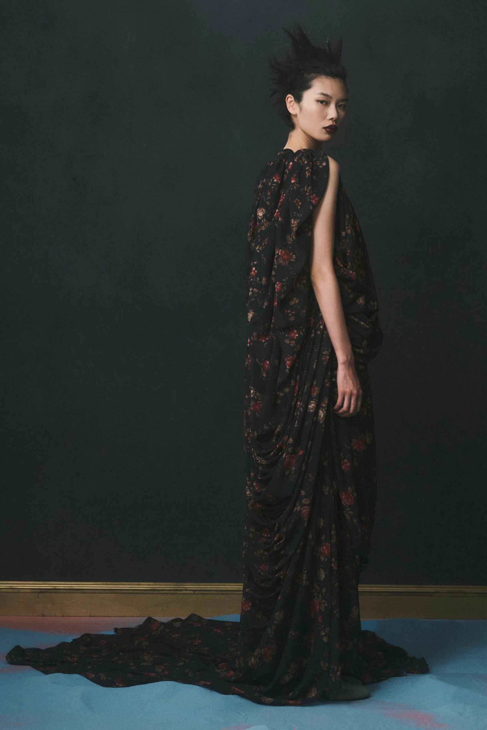 Black floral chiffon gown draped into deep swags, one side entirely sleeveless. After midnight in a museum period room, velvet ropes finally unhooked.