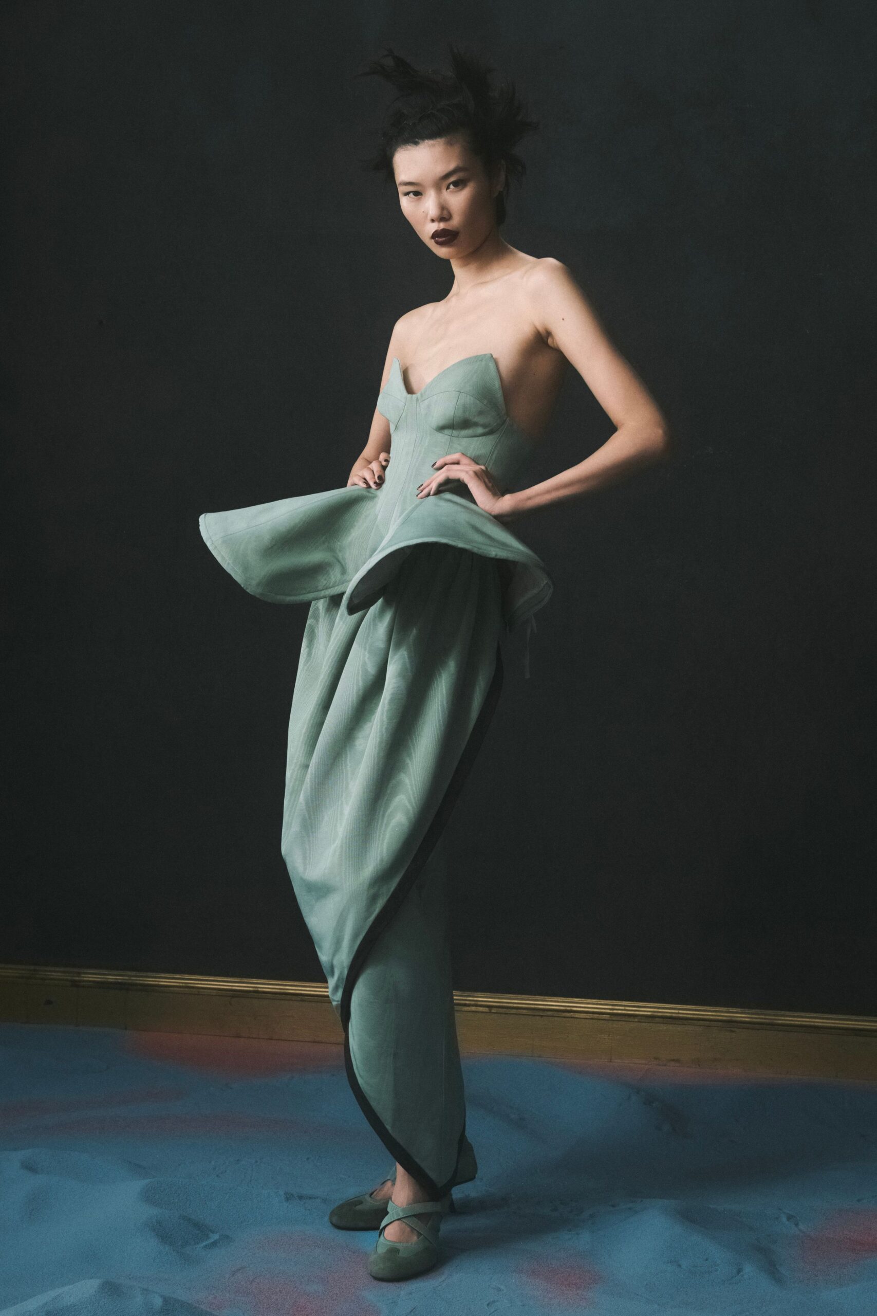 Seafoam moire dress with a pointed sweetheart bodice and winged peplum flare. Matching satin flats with crossed straps over the instep. Crossing a faded theater stage before the house lights come up.