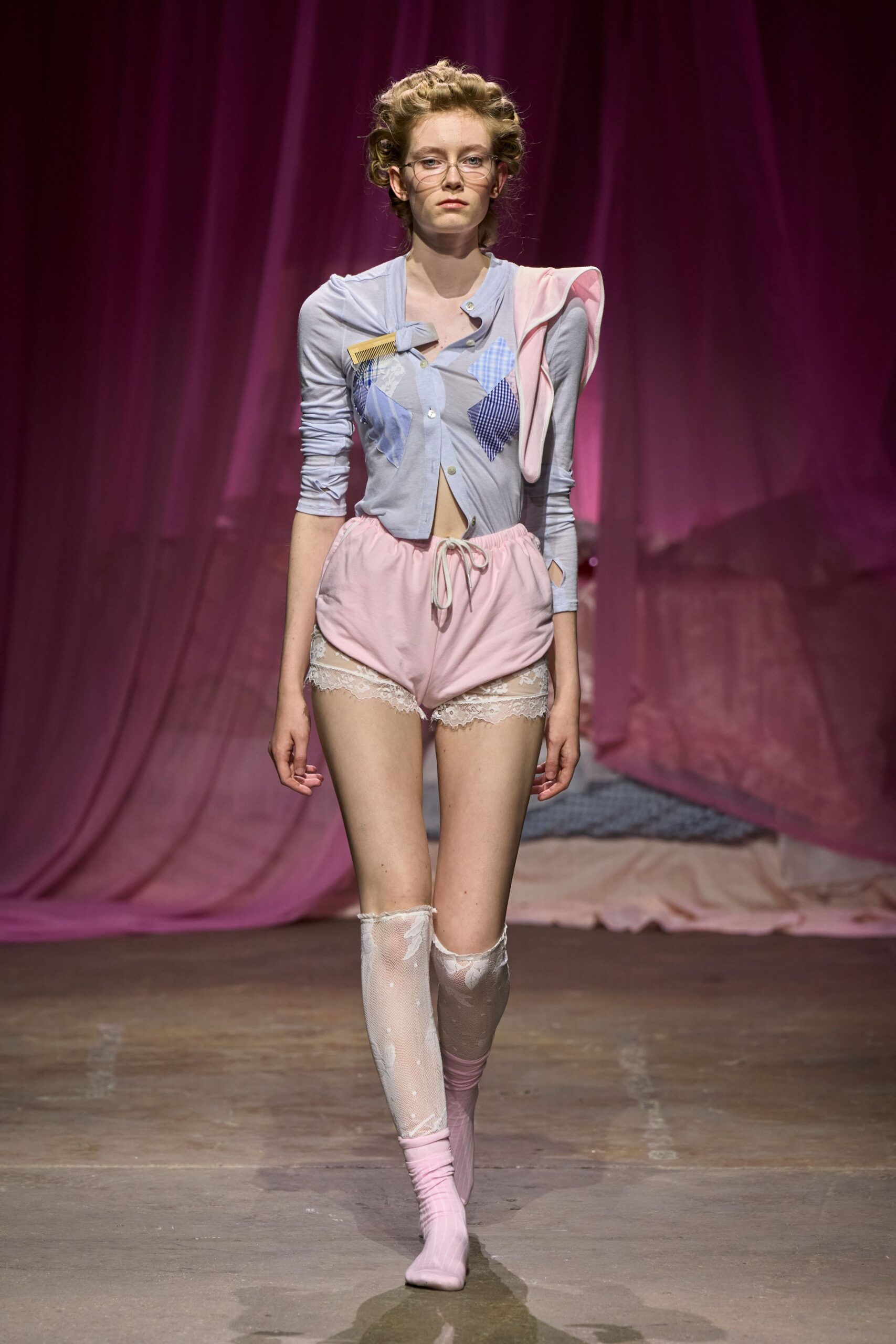 Thin wire frames. Powder-blue knit cardigan pieced with gingham diamonds and a clipped comb. Blush tap shorts with a white drawstring and lace peeking below. Mismatched white lace stockings, one slouched at the calf. Pink sock heels. For padding to the kitchen at noon in somebody else's apartment.