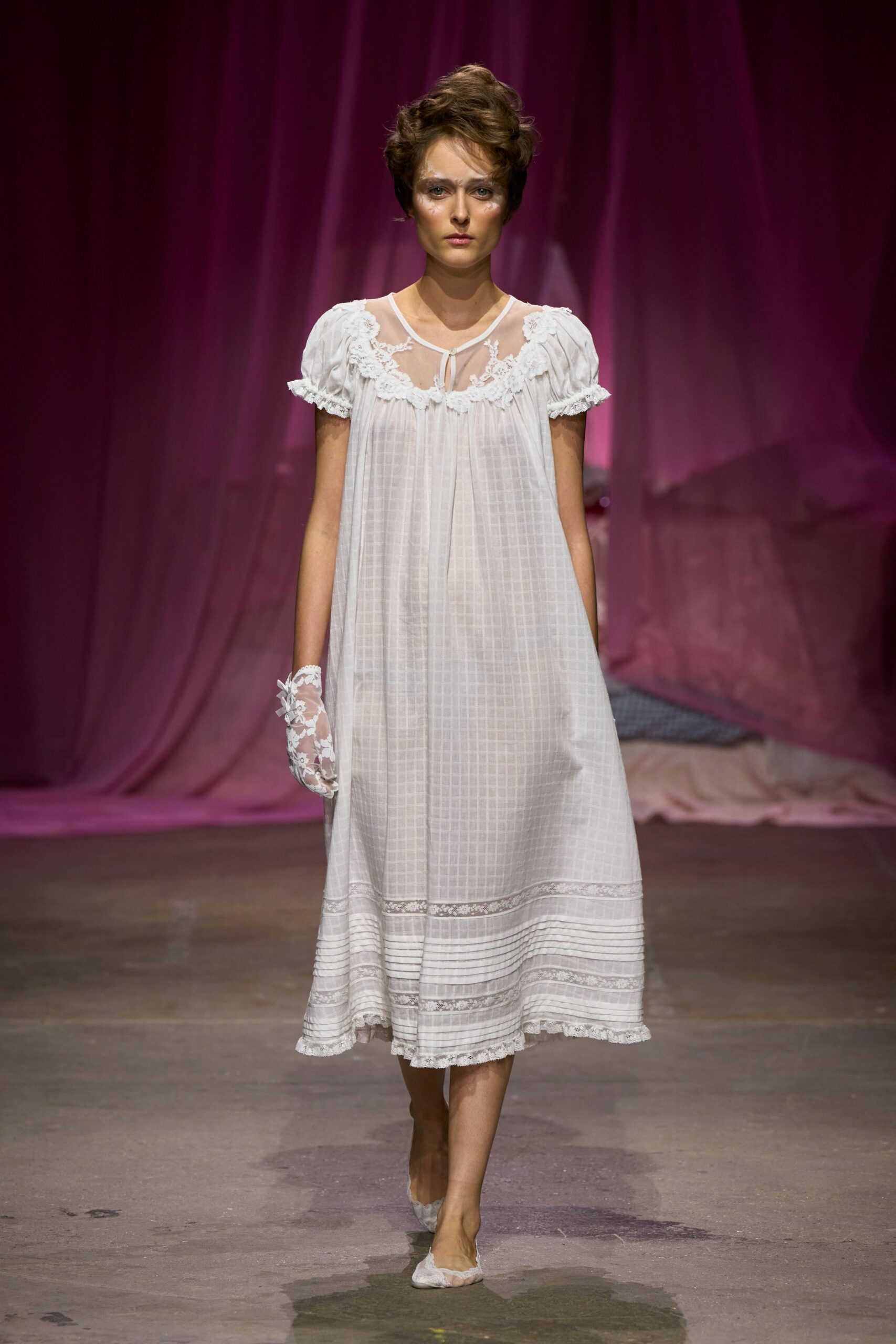 White checked cotton nightdress, sheer yoke edged in floral lace. Single white lace glove with scalloped cuff on the left hand. White lace flats cut low across the toes. Early morning in a boarding house, crossing the hall before anyone wakes.