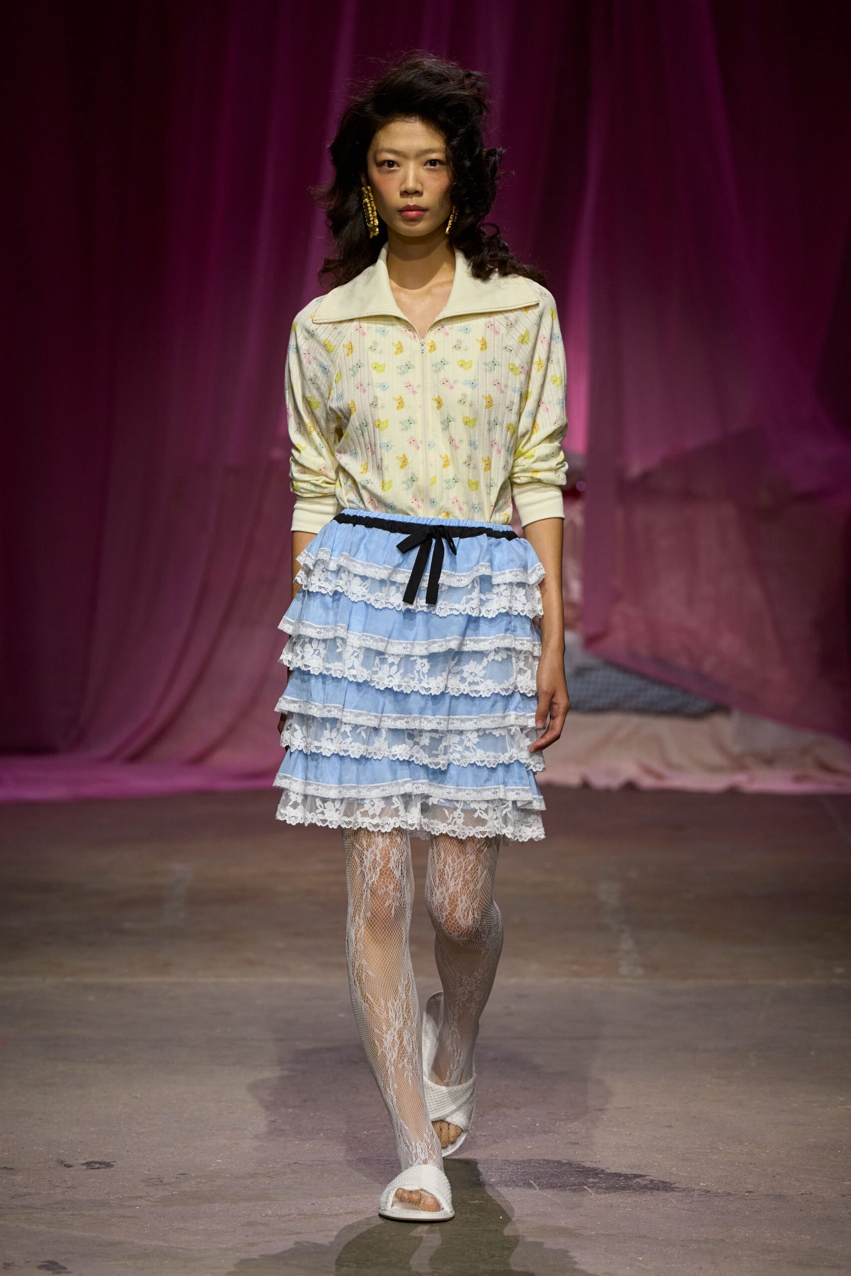 Cream ribbed zip top scattered with tiny pastel animal motifs. Powder-blue skirt built in tiered ruffles, each band edged in white lace. White lace-pattern fishnet tights. White woven peep-toe mules. Sunday morning hotel breakfast, still wearing last night's teased hair.