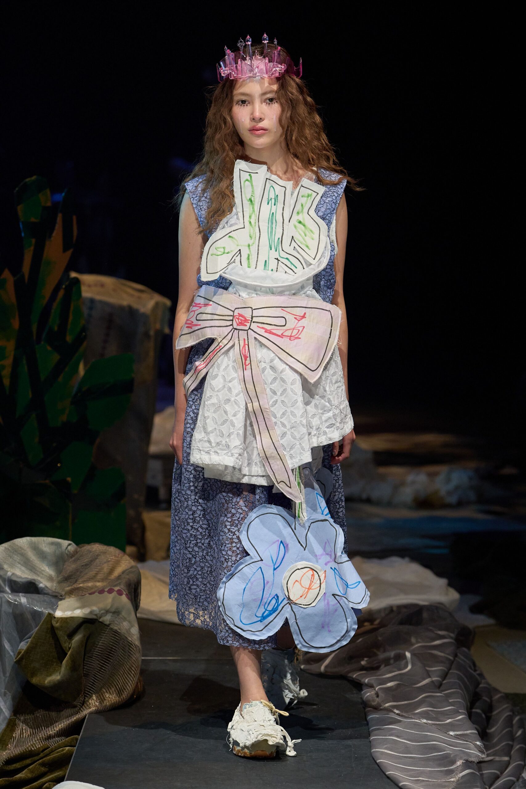 Blue floral lace dress layered with a white eyelet apron, topped by hand-drawn appliques: a ribcage bib, oversized pink bow and drooping flower bag. Pink translucent crown, frayed white shoes. After the school play, still in costume.