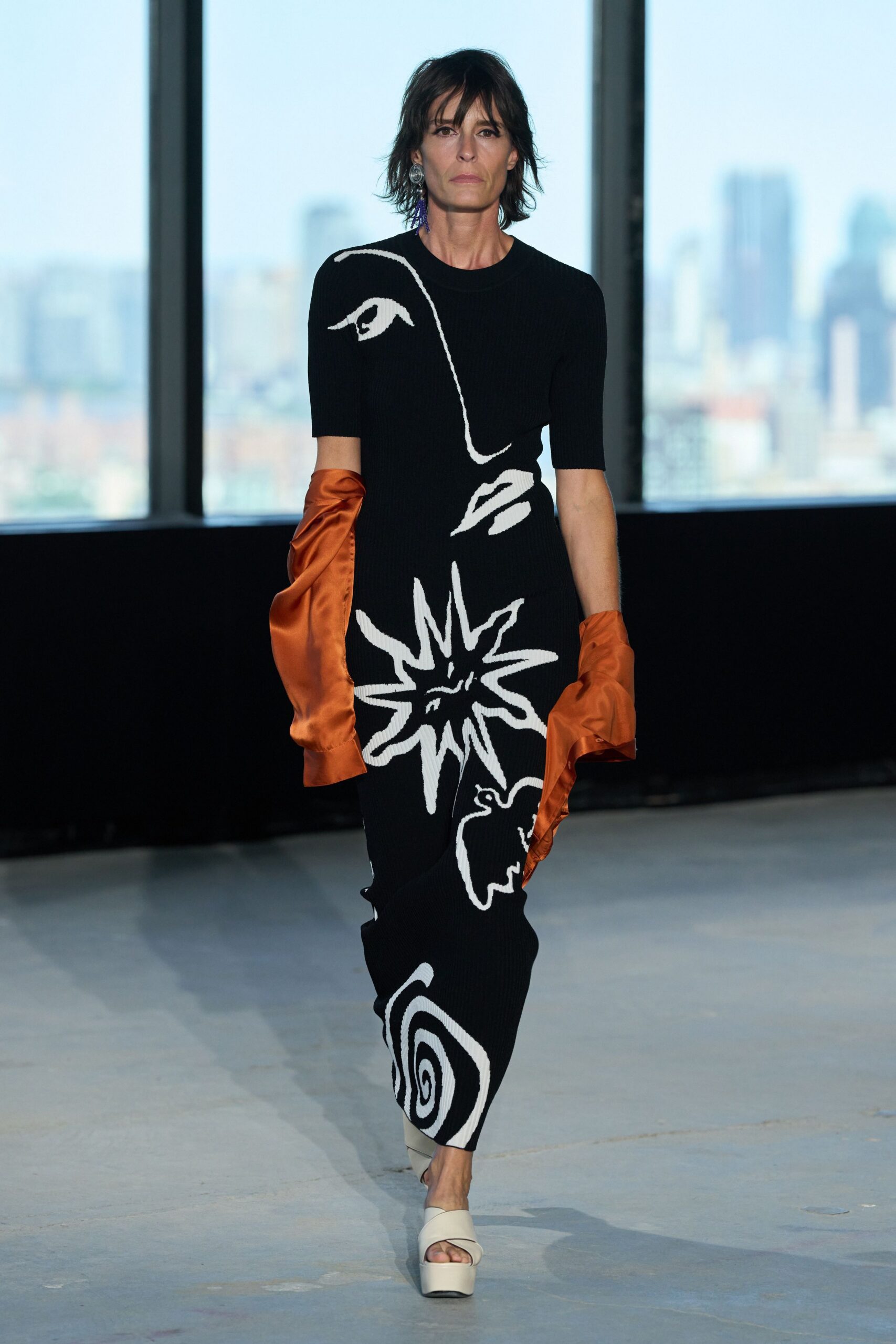 Black ribbed column dress with white abstract intarsia and elbow sleeves. Burnt orange satin opera gloves, softly collapsing at the wrists. Ivory leather platform mules with a broad twisted front band. One violet tassel earring. Walking into a high-rise cocktail party before the windows turn black.