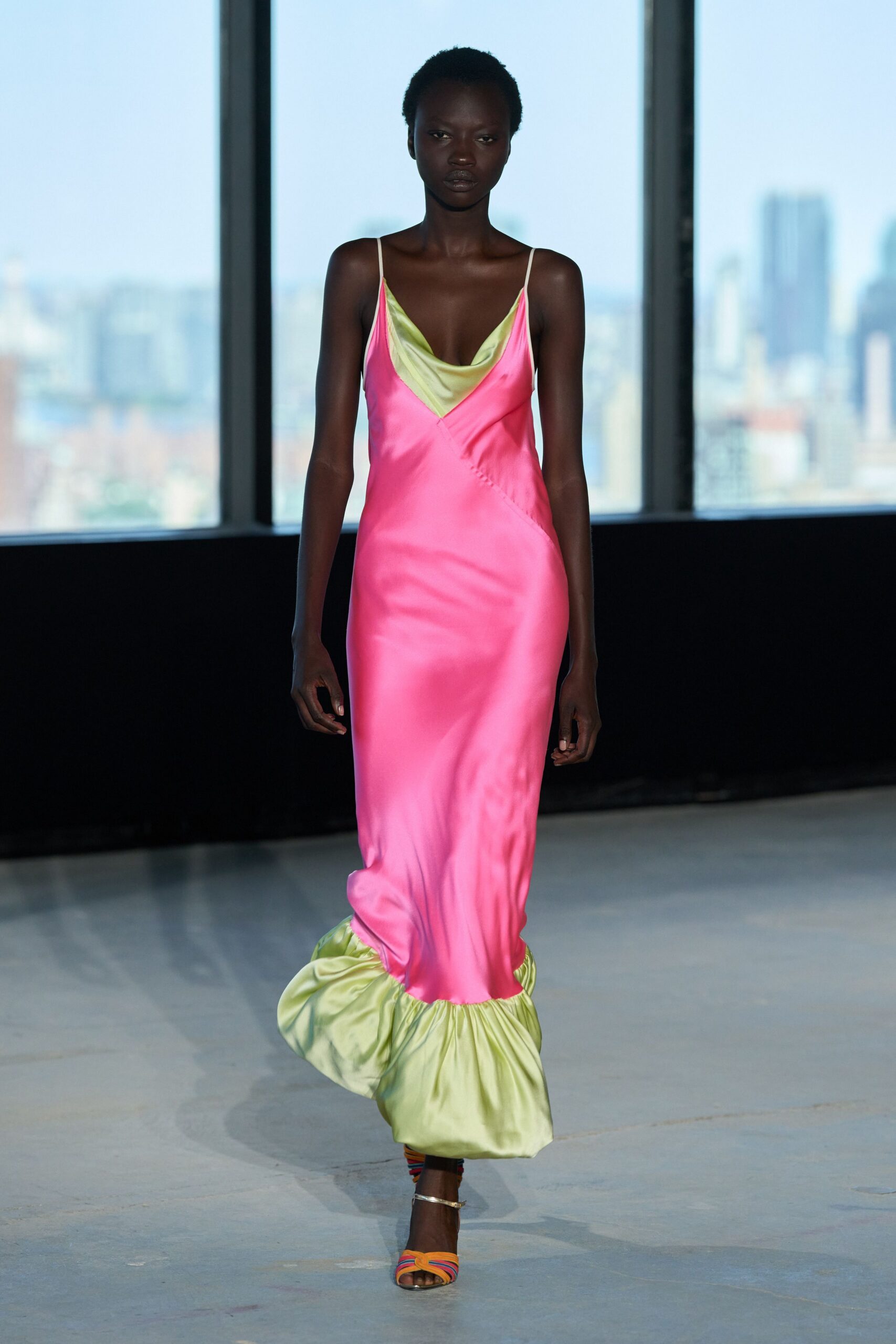 Hot-pink satin slip dress with chartreuse cowl inset and ruched fishtail hem. Rainbow corded sandals with a thin gold ankle strap. Rooftop wedding after the sun drops, city still pale beyond the glass.