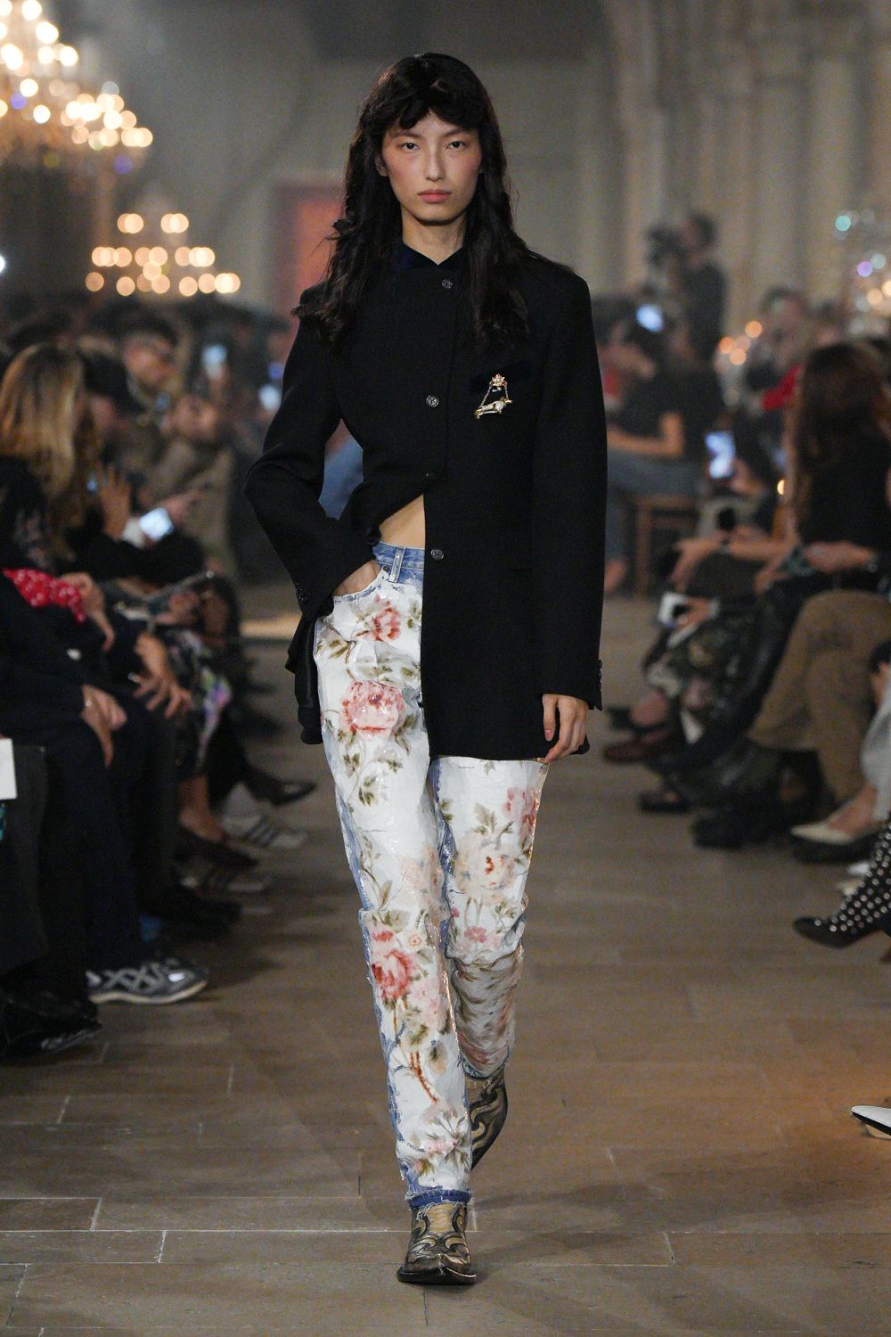 Long black blazer, cut away at one side with a jeweled insect pin. Sheer white trousers washed with blown-up roses over pale denim panels. Pointed ankle boots in muddied scroll print. Crossing a drafty manor corridor before the candles burn down.