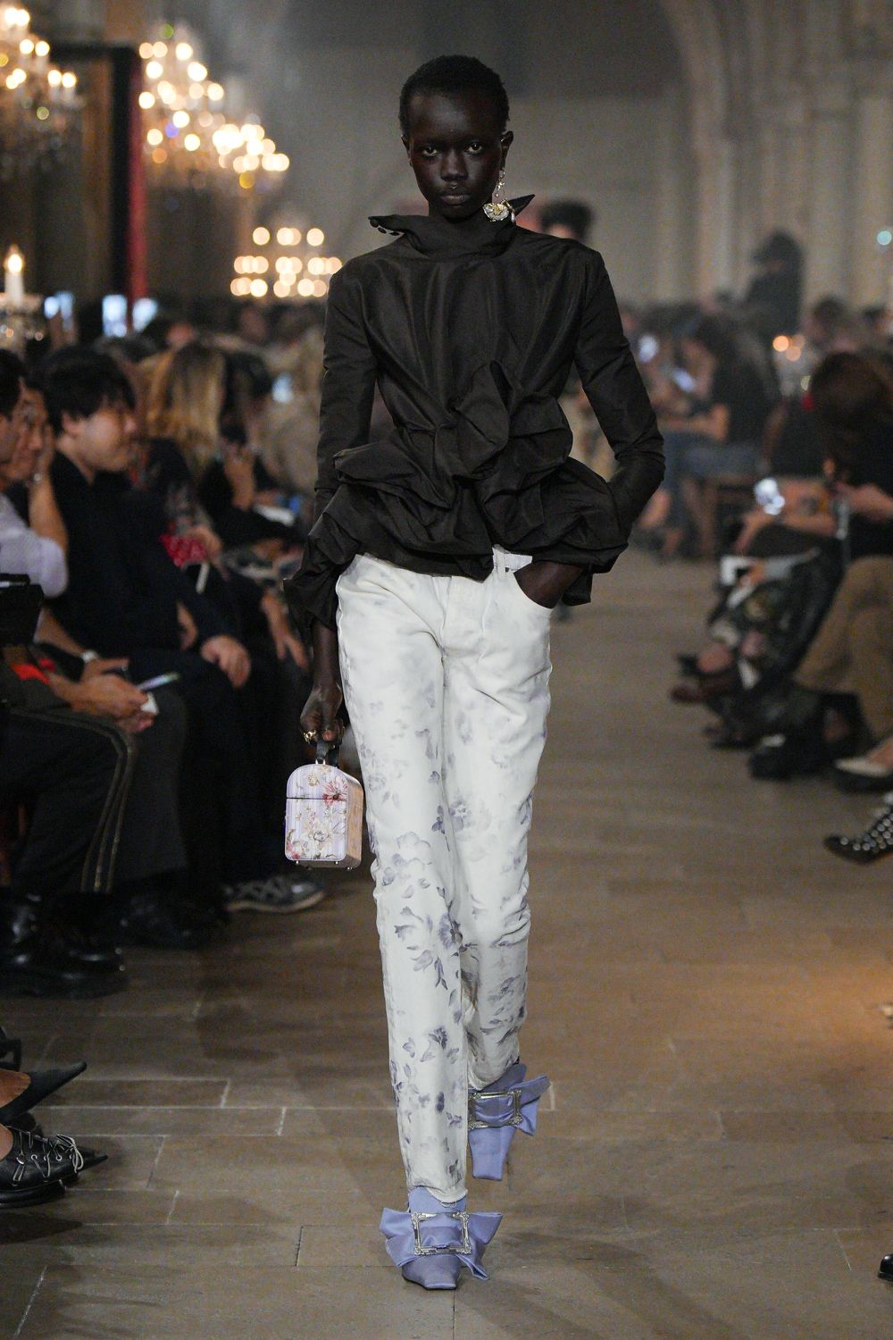 Black taffeta blouse with a high collar and spiraling ruffles. White slim trousers washed with pale grey floral shadow prints. Hard case mini bag in faded floral brocade. Powder-blue satin pumps with oversized crystal buckle bows. Walking through a candlelit manor after the dessert plates are cleared.
