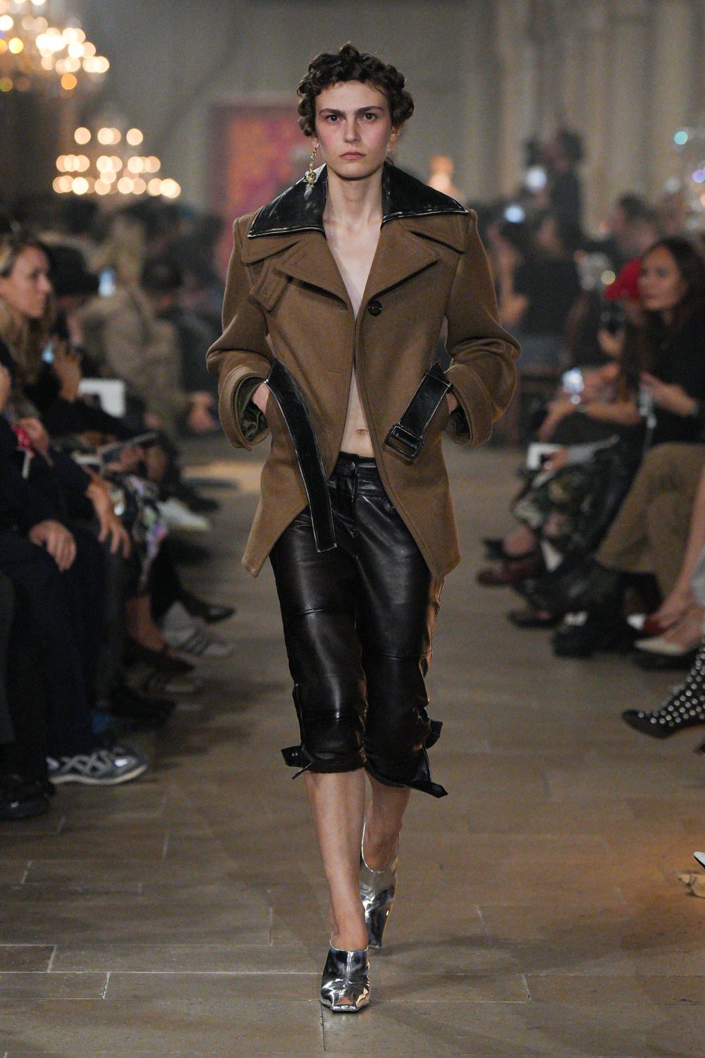 Tobacco wool coat with a glossy black patent collar and dangling cuff straps. Black leather capris, seamed through the knee and buckled at the calf. Crushed silver pumps with sharp squared toes. Mismatched dangling metal earrings. Whatever you wear to smoke on the terrace after the house wedding dinner.
