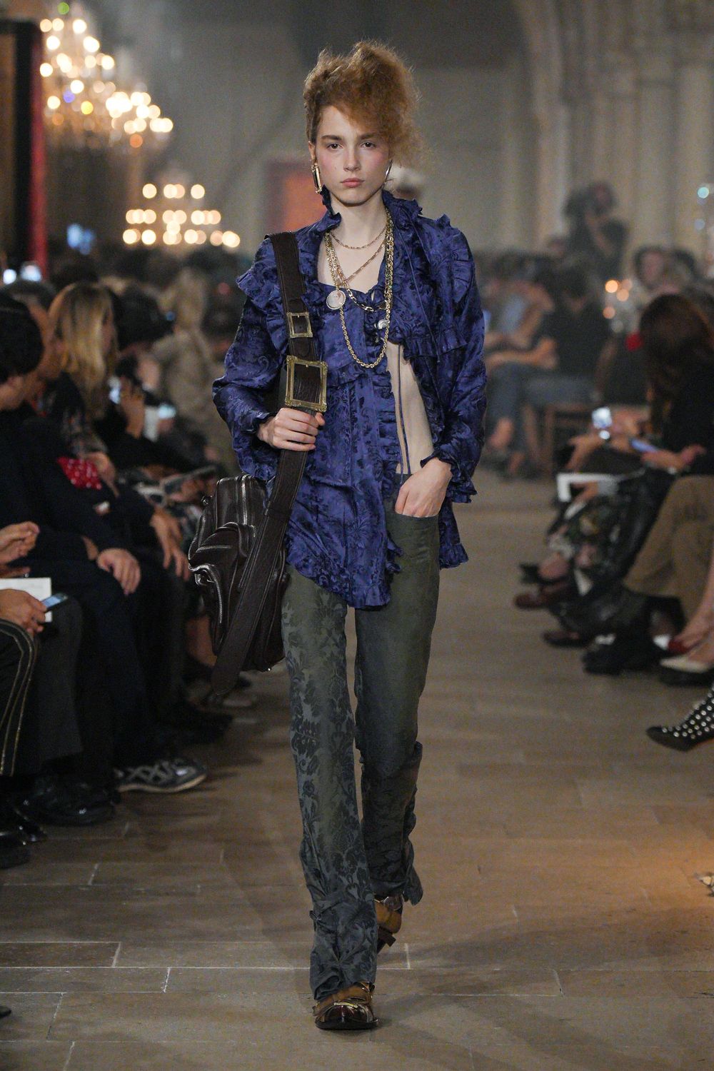 Cobalt jacquard ruffle blouse, one side falling open over a nude panel. Olive damask trousers, extra length ruched into the ankles. Dark leather shoulder bag on a wide strap with oversized brass frames. Brown loafers with tasseled vamps. Crossing a drafty manor hallway after everyone else has gone to bed.