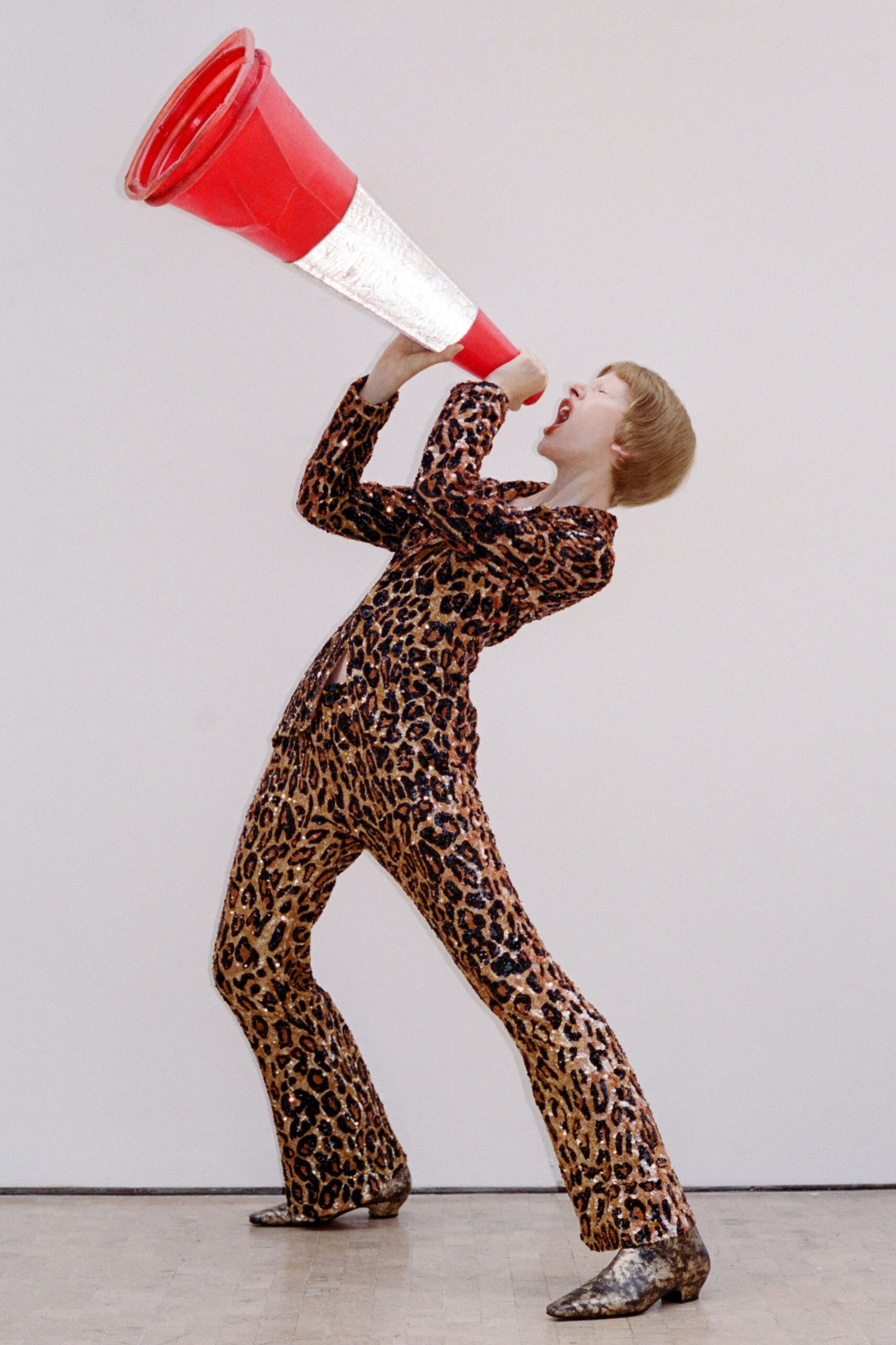 Leopard sequined blazer, cut close through the waist with black buttons. Matching flared trousers, sequins catching copper and black with each step. Silver crushed-leather ankle boots with low Cuban heels. Shouting through a practice cone at an empty gym after school.