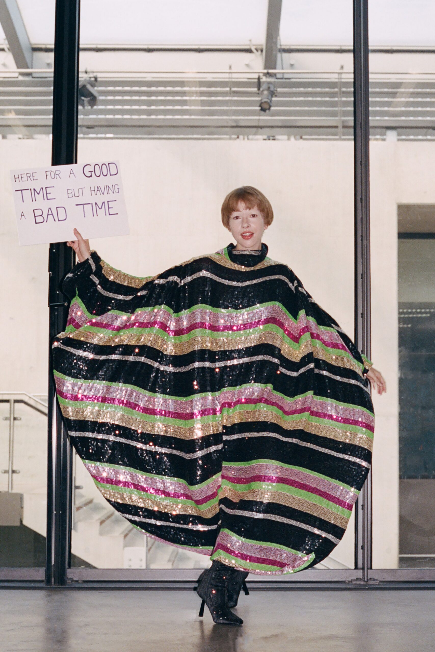 Ballooning black sequined caftan banded in lime, fuchsia, silver and gold stripes. Black glitter ankle boots with narrow heels peeking from the hem. Holding a protest sign at the office party after midnight.