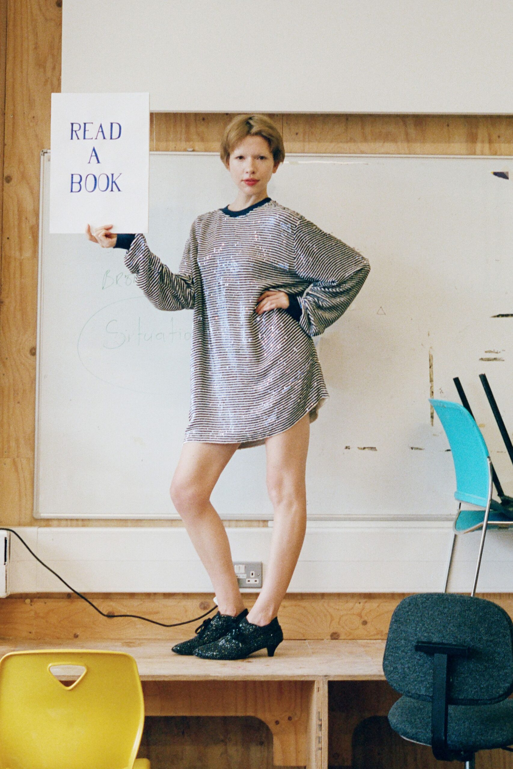 Oversized silver sequin sweater dress, black ribbed collar and cuffs. Black glitter lace-ups on a low kitten heel. Standing on the classroom platform after volunteering to read aloud.