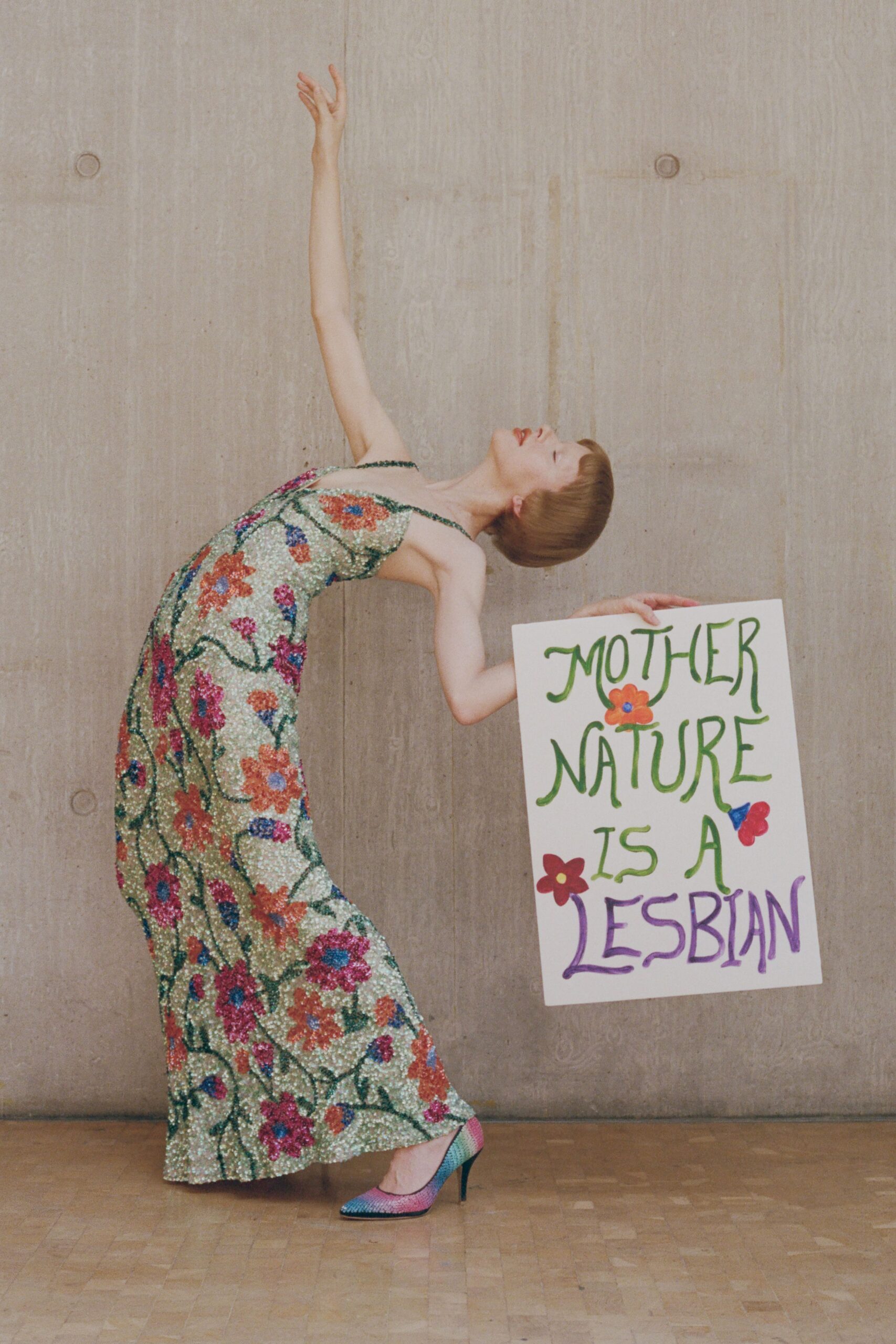Spaghetti-strap column dress crusted in pale green sequins with beaded flowers. Pointed pumps shaded from pink to turquoise rhinestones. Holding a handmade rally sign after the march has gone indoors.