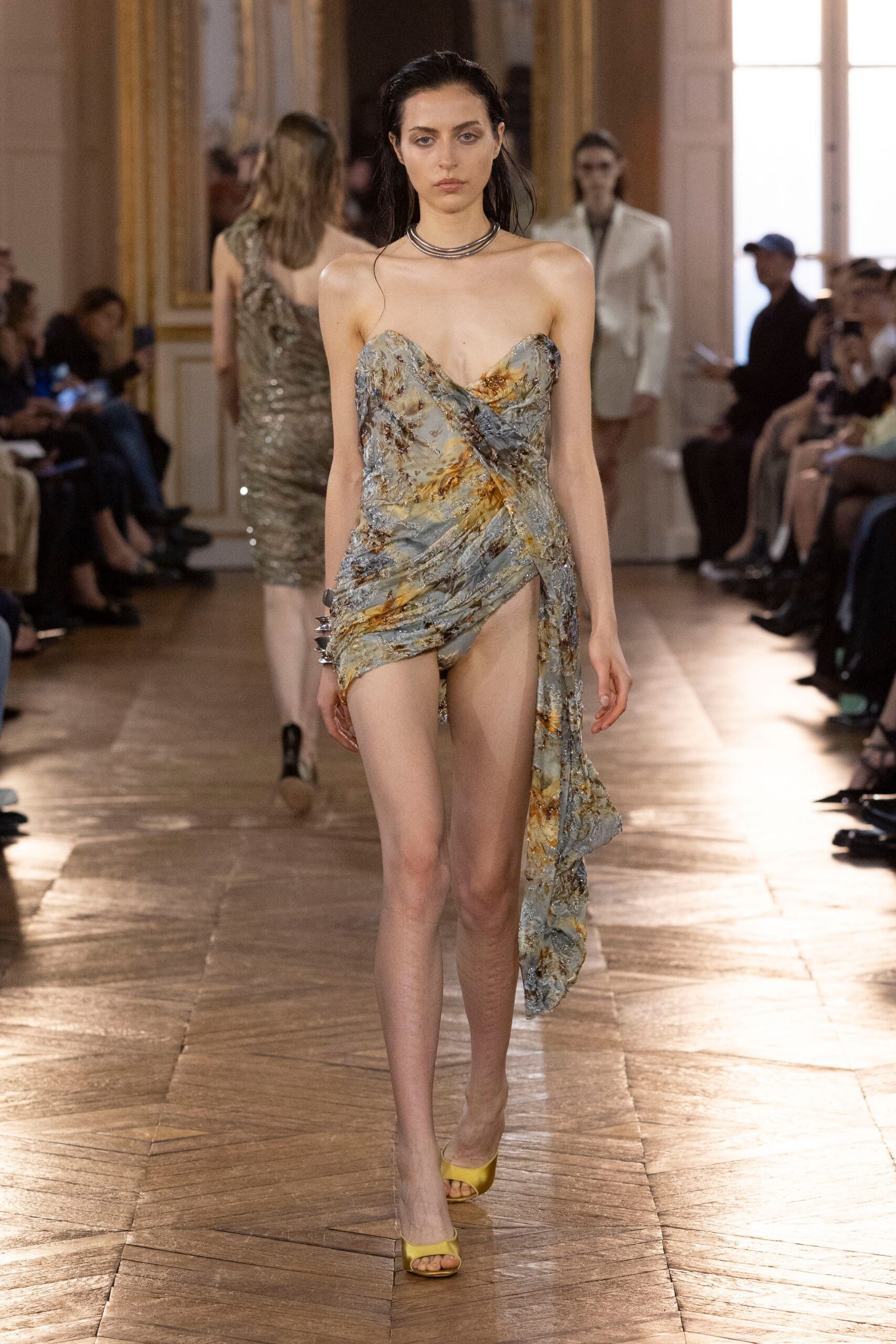 Stacked silver torque choker hugging the collarbones. Strapless draped dress in crushed devore, rust blooms across pale blue. Spiked silver cuff at one wrist. Chartreuse satin peep-toe mules. The hour after a bathhouse closes, still damp under the marble lights.