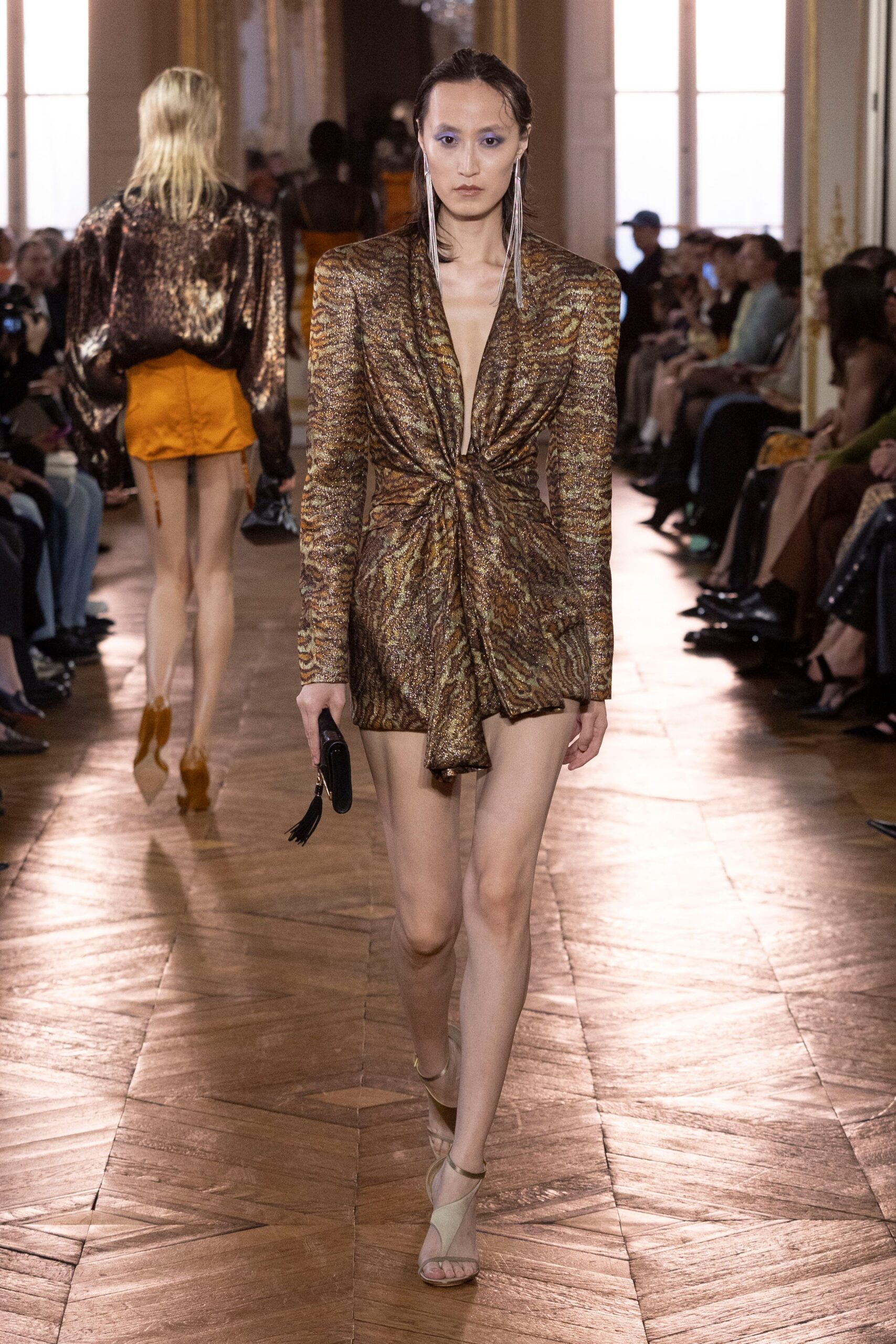 Bronze zebra-jacquard mini dress, plunging V twisted tight at the waist. Long silver fringe earrings grazing the collarbone. Black cylinder clutch with a short tassel swing. Nude mesh sandals with narrow metallic straps. Crossing a hotel ballroom after midnight, still carrying the room key.