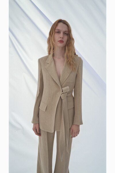 Oatmeal blazer cut low at the chest, cinched with a long self-tie. Matching straight trousers in faintly slubbed suiting cloth. For the meeting that turns into drinks before anyone goes home.