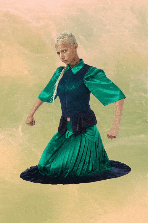 Emerald satin shirt dress with a sharp collar and wide elbow sleeves. Black fitted bodice over it, peplum jutting out at the hips. Knife-pleated skirt pooling into a dark circular hem. Kneeling in wet grass after the garden party has already packed up.