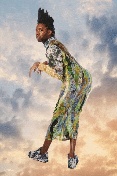 Long printed column dress in sliced chartreuse panels and grey toile swirls. One yellow lace sleeve, dense like netted sequins at the wrist. Grey-and-black toile sneakers with thick white soles. Crossing a rooftop at dusk while the storm light turns peach.