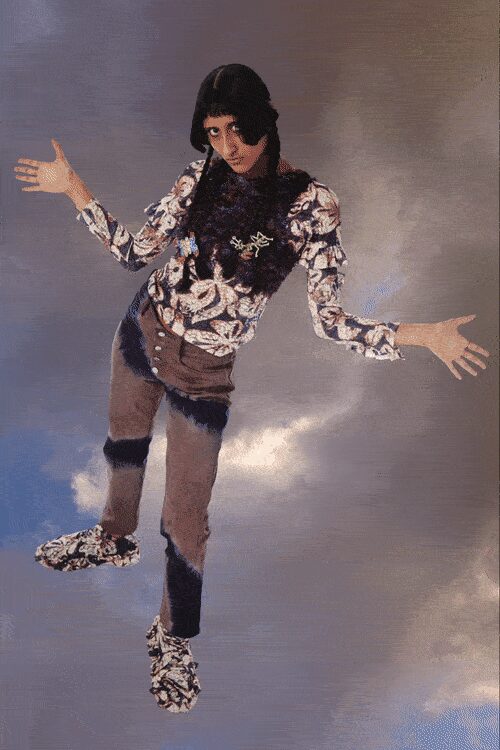Cream and brown swirl-print knit top with a dark fur chest panel. Taupe skinny trousers broken by black fuzzy bands at hip, knee and cuff. Matching swirl-print shoes, soft and slipper-like. Crossing a motel parking lot after rain, still wearing yesterday's eyeliner.