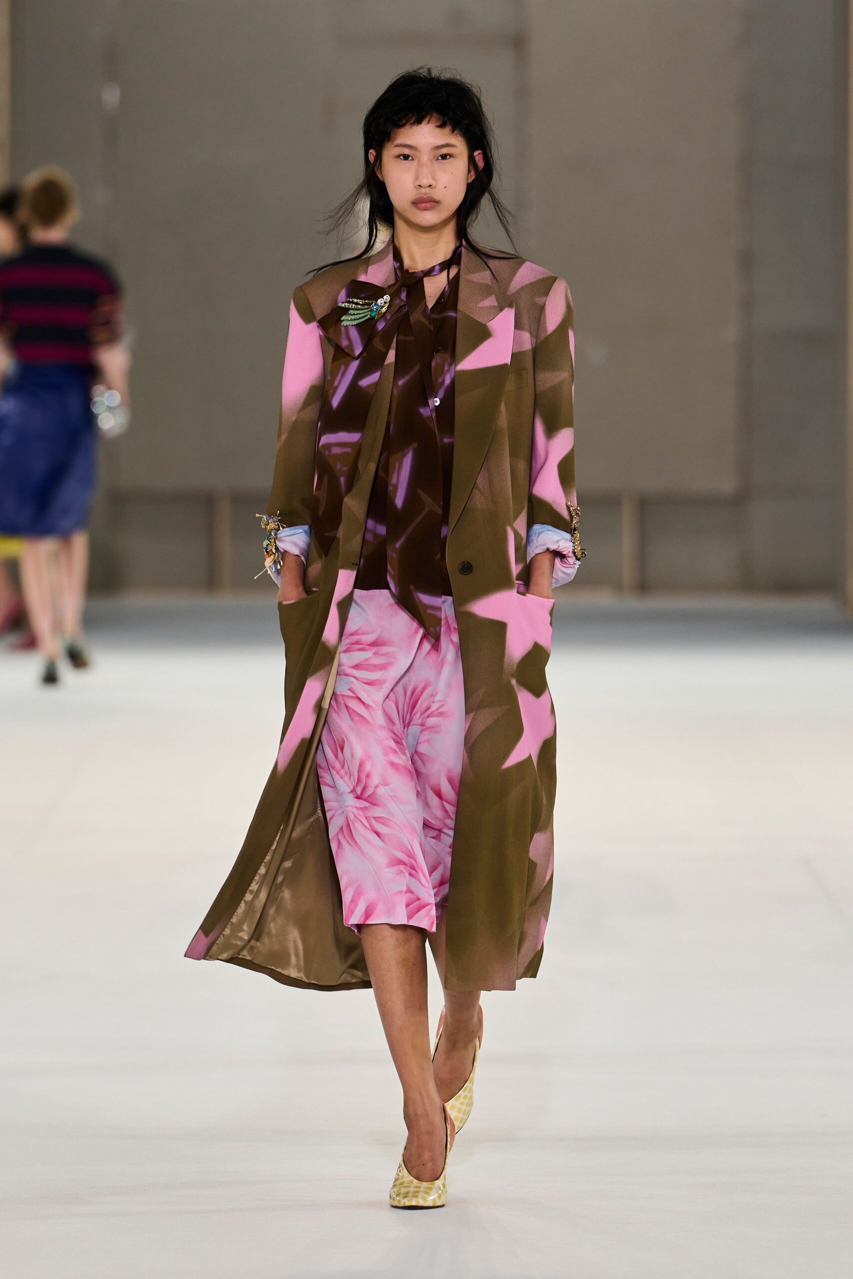 Long olive coat splashed with pink, pale blue cuffs pinned with jeweled sprays. Glossy brown blouse with a loose scarf tie and violet shard print. Pink knee-length shorts printed with swirling chrysanthemum petals. Yellow snakeskin pumps. Walking into a hotel atrium with florist paper still rustling under your arm.
