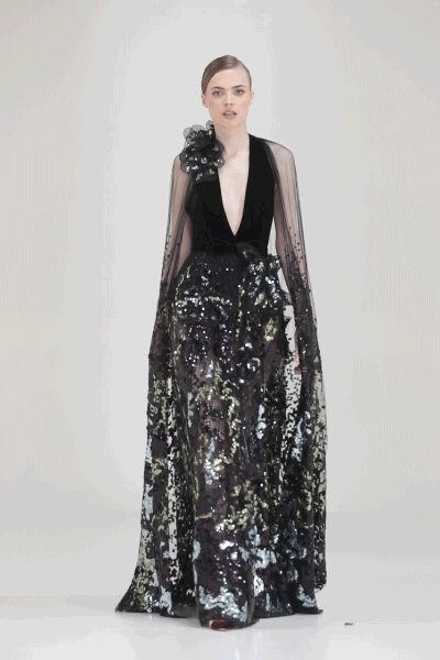 Plunging black velvet bodice with sheer beaded sleeves and a rosette shoulder. Floor-length paillette skirt in black and silver, pooling heavily at the hem. The charity ball has ended and the marble stairs are finally empty.