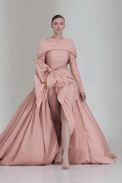 Blush satin gown with a folded bateau drape and one colossal hip bow. Ruched long sleeves fitted close to the arm. Split front overskirt falling into knife pleats and a sweeping train. Blush boots, squared off at the toe. For crossing a ballroom after everyone has already seen you cry.