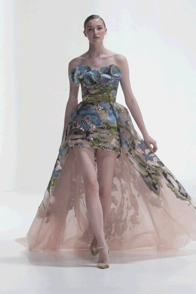 Strapless blossom-painted mini with a boned bodice and trailing blush tulle overskirt. Pale green ankle-strap pumps with pointed toes. Crossing a hotel ballroom after the wedding band has packed up.