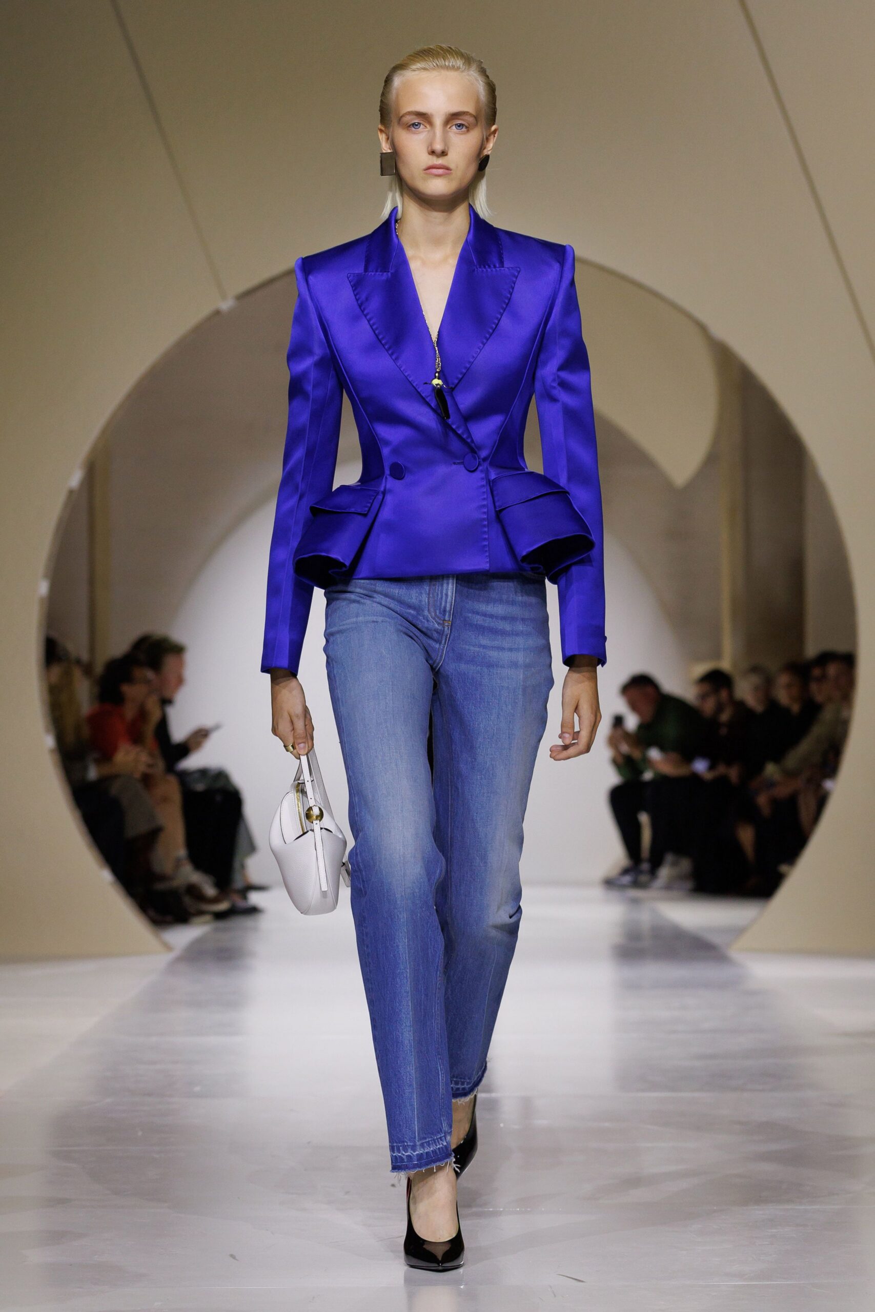 Electric-violet satin blazer, peaked lapels and flared peplum pockets. Pale stonewashed jeans with a frayed hem brushing the shoe. White top-handle bag with a brass sphere at the strap. Black patent pumps, sharply pointed. Walking into a courthouse wedding with the paperwork already signed.