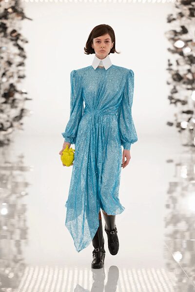 Icy blue glittered dress, white point collar and one draped handkerchief panel. Tiny citron cluster bag. Black buckle-strap boots with a clunky shine. Crossing a hotel atrium before noon with flowers bought downstairs.