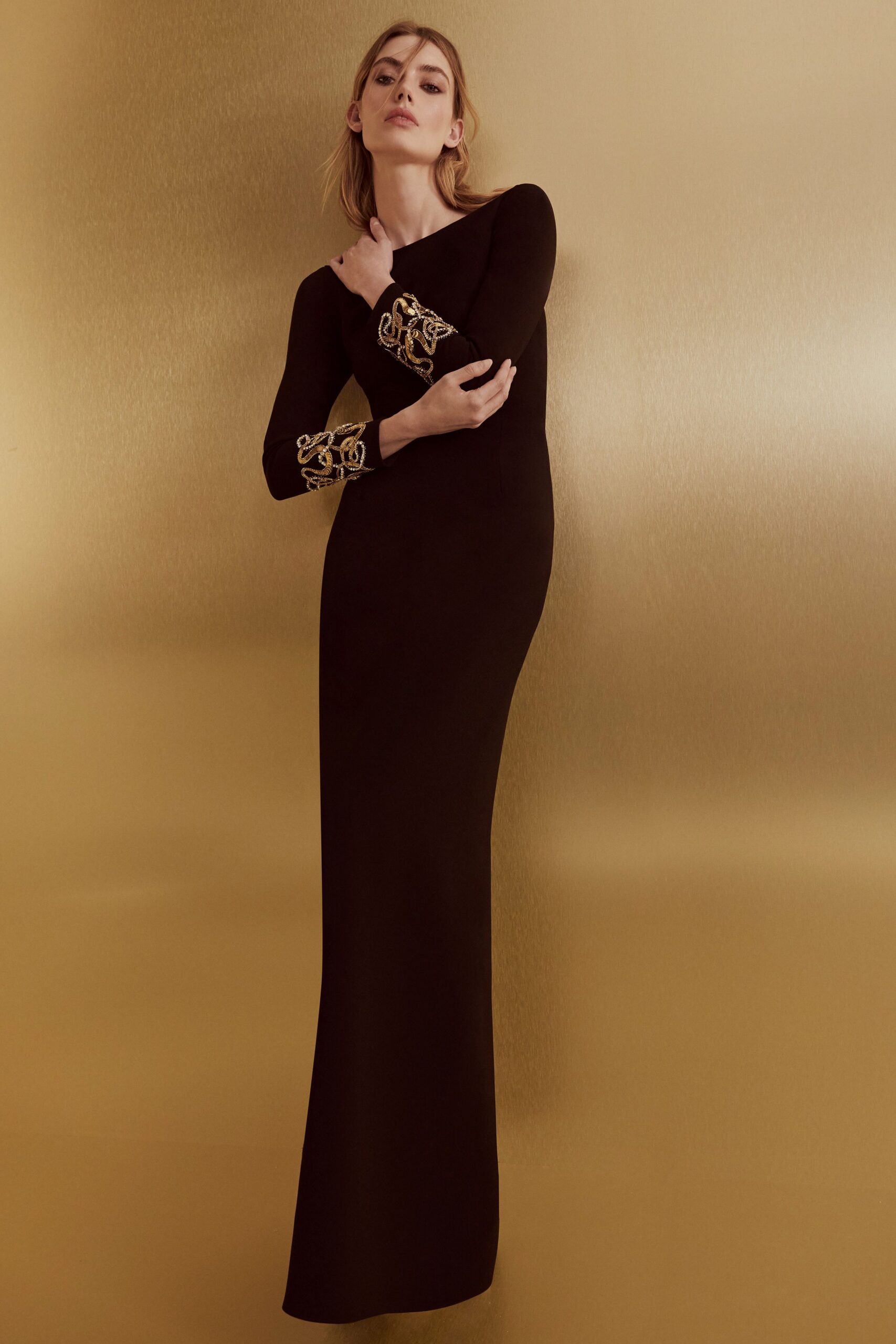 Black column gown with a bateau neckline and gold cord embroidery at the cuffs. At the embassy reception when the string quartet starts tuning.