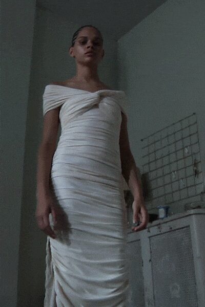 Ivory jersey column dress, ruched through the body with an off-shoulder twisted neckline. In a rented flat kitchen after midnight, barefoot except for the cold tiles.