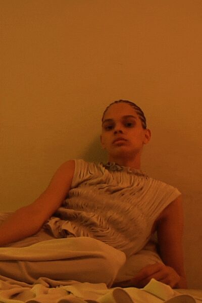 Stone draped top with cap sleeves and rippling ruched channels. Cream wide trousers in a fluid weave, pooling across the seat. Heat still trapped in the walls after everyone else left.