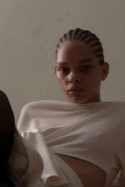 Ivory jersey top draped high across the collarbone with a side cutout. Morning light in an empty apartment before the sheets are off the sofa.