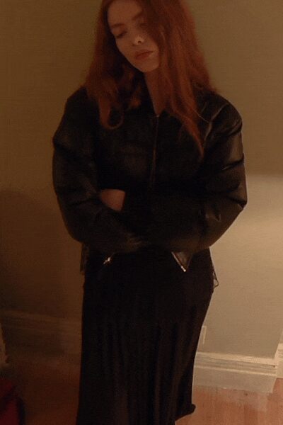 Black leather jacket with rounded sleeves and a zip flashing at the hip. Black pleated midi skirt falling in narrow vertical folds. Whatever you wear home when the party thinned to two people.