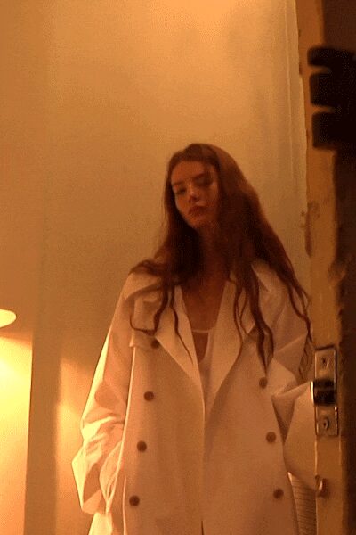 Oversized ivory double-breasted coat with broad lapels and caramel horn buttons. White scoop-neck layer peeking through the deep open front. Opening the hotel room door at sunrise, still in yesterday's makeup.