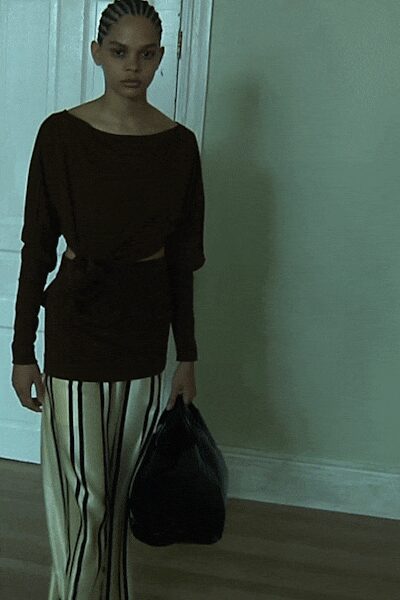 Dark draped jersey top, one side knotted into a waist cutout. Ivory trousers with long black vertical stripes, loose through the leg. Slouchy black leather holdall. Whatever you throw on to collect keys from an almost empty flat.