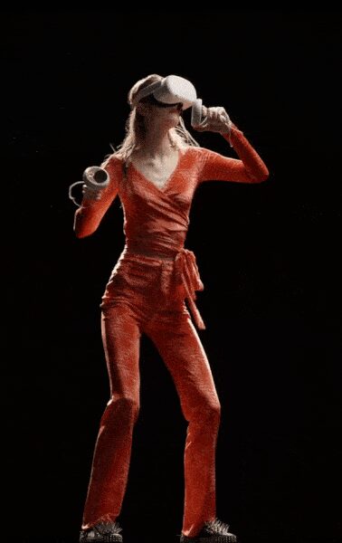 White visor pulled low, black band wrapping behind the head. Burnt orange ruched knit wrap top with a deep V. Matching flared knit trousers, side tie knotted high on the hip. Spiky silver shoes. Holding two coffees while the gym juice bar opens its shutters.