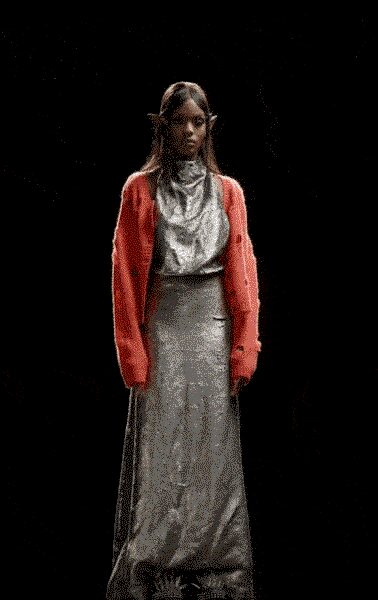 Coral knit cardigan hanging open, sleeves slouched past the wrists. Silver liquid-lamé draped top with a loose cowl neck. Floor-length pewter satin skirt, falling straight from a high waist. Hotel corridor at dawn, still in last night's jewelry and somebody else's knit.