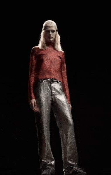 Pale mesh headscarf stretched close over the crown. Rust red long-sleeve top with a crackled, reptile-skin sheen. Silver metallic trousers, creased hard through the front. Pointed silver shoes, mostly swallowed by the hem. Crossing an empty casino floor after sunrise.