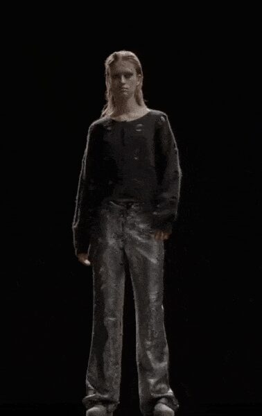 Black knit sweater with a wide boat neck and scattered eyelets. Silver foil trousers, creased straight through the leg. White rounded shoes peeking under the hem. Whatever you wear home after the club lights come up.