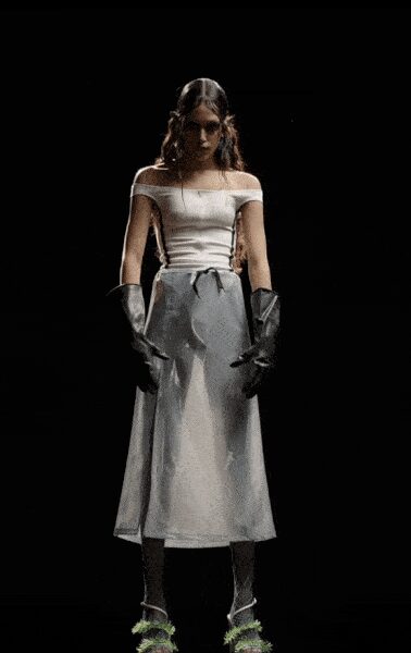 Off-shoulder ivory knit top with a long center seam. Silver satin midi skirt, tied with a narrow black cord. Black opera gloves in glossy leather. Sheer black stockings. Ankle-strap heels with acid-green feathered fronts. Whatever you wear home when the gala spilled into morning.