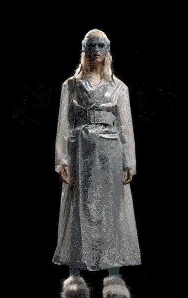 Translucent blue wraparound visor obscuring the eyes. Pearl-grey satin trench, broad lapels and a self belt knotted low. Loose matching satin trousers breaking softly over the feet. White furry slippers, thick and cloudlike. Crossing a dark hotel corridor after the spa closed hours ago.
