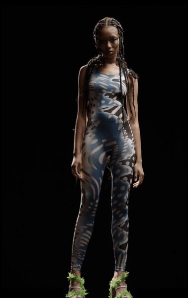 Second-skin sleeveless catsuit in cloudy blue stretch jersey, mottled with pale blotches. Clear platform heels trimmed with sharp tufts of acid-green marabou. Under the planetarium dome after hours, still wearing the ticket wristband.